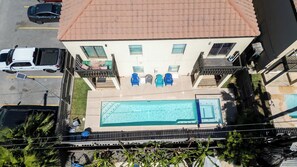 A two-story building with a rooftop pool, a covered patio with chairs, and a parking area. - Near Beach Retreat - Ground Floor - Pool - Walk to All (South Padre Island)
