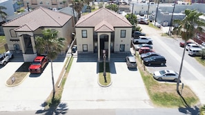 Um edifício de dois andares com telhado em telhas, entrada central e um estacionamento com vários carros.