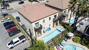 A hotel with a swimming pool, multiple cars parked in the lot, and a clear view of the surrounding area. - Near Beach Retreat - Ground Floor - Pool - Walk to All (South Padre Island)