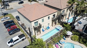 A hotel with a swimming pool, multiple cars parked in the lot, and a clear view of the surrounding area. - Near Beach Retreat - Ground Floor - Pool - Walk to All (South Padre Island)