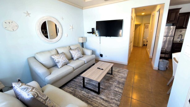 A living room with a sofa, coffee table, and a TV mounted on the wall. - Near Beach Retreat - Ground Floor - Pool - Walk to All (South Padre Island)