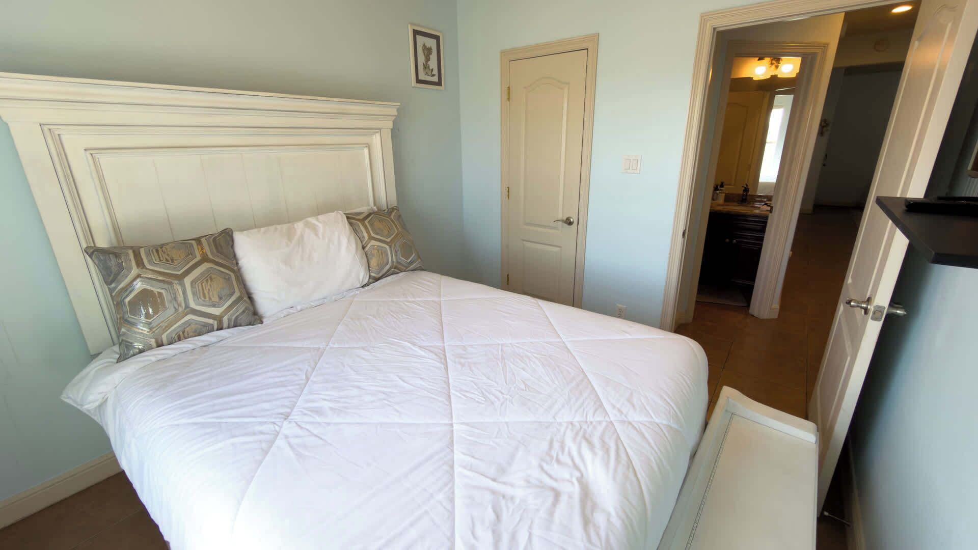 A bedroom with a bed, a door, and a hallway leading to a bathroom.
