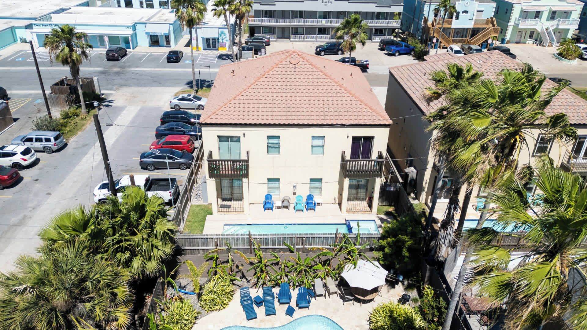 A hotel with a swimming pool, multiple balconies, and parked cars.