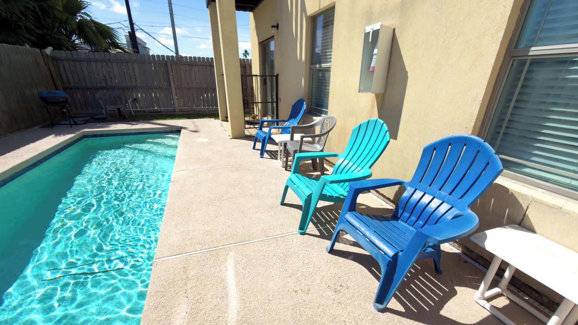 A swimming pool with blue chairs and a white table.