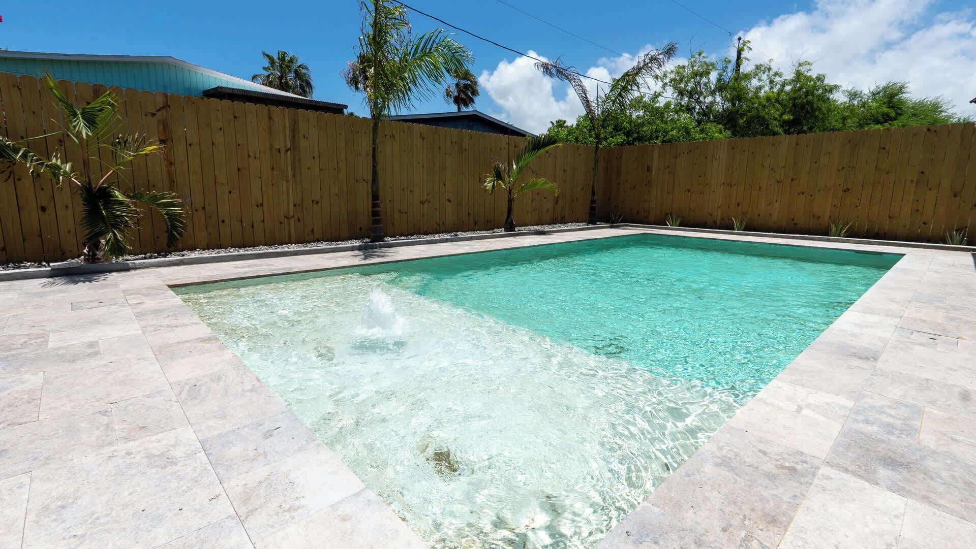 A rectangular swimming pool with clear water, surrounded by a wooden fence and a tiled deck.