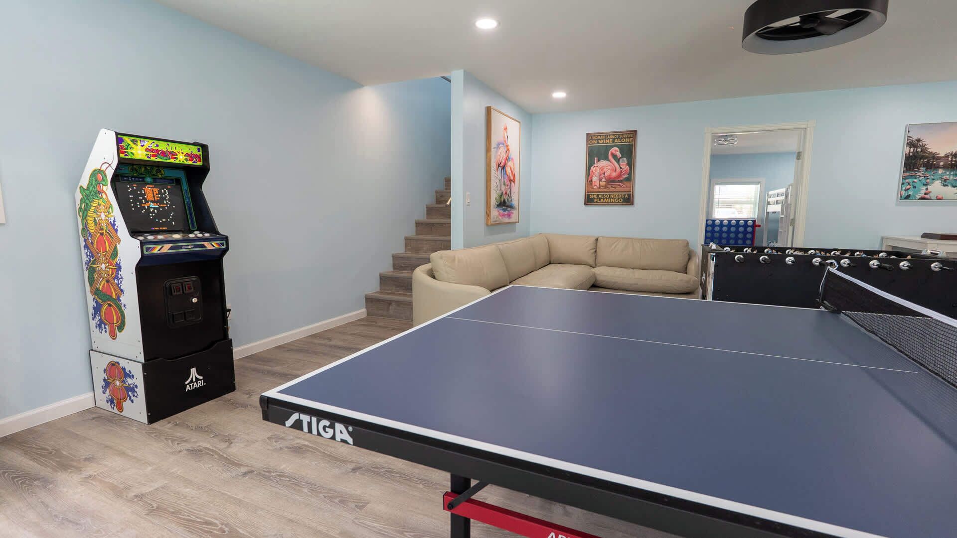 A room with a ping pong table, a gaming console, a sofa, and a staircase.