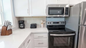 Uma cozinha com armários brancos, cafeteira, torradeira, micro-ondas, forno e geladeira.