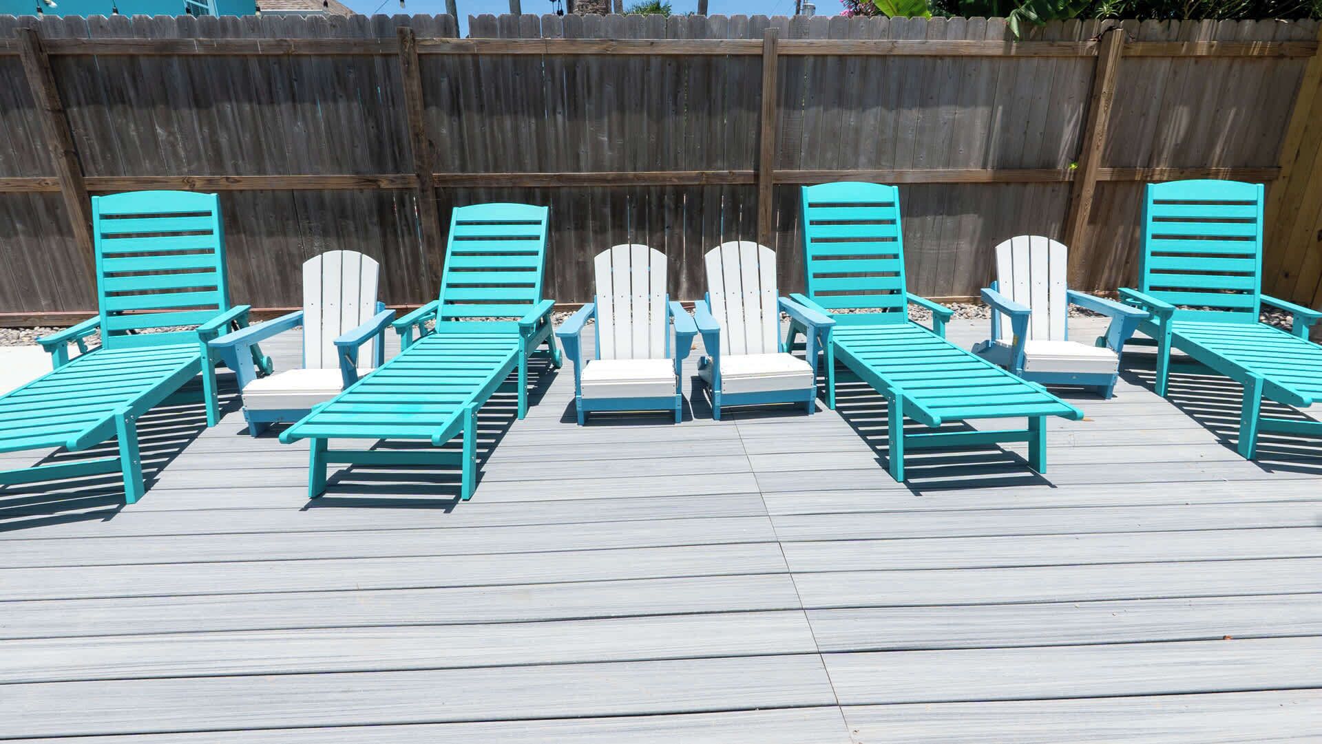 Eine Terrasse mit mehreren türkisblauen Liegestühlen und weißen Kissen.
