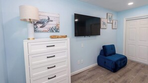 A room with a white dresser, a blue chair, a flat-screen TV, and artwork on the wall. - New 5BR Remodel, Heated Pool, Game Room (South Padre Island)