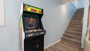 A retro arcade machine in a hallway with a wooden staircase. - New 5BR Remodel, Heated Pool, Game Room (South Padre Island)