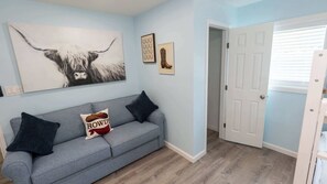 Habitació amb un sofà gris, dos coixins negres, un coixí amb tema Howdy i una obra d'art gran amb el rostre d'una vaca, més una porta que condueix a una altra habitació.