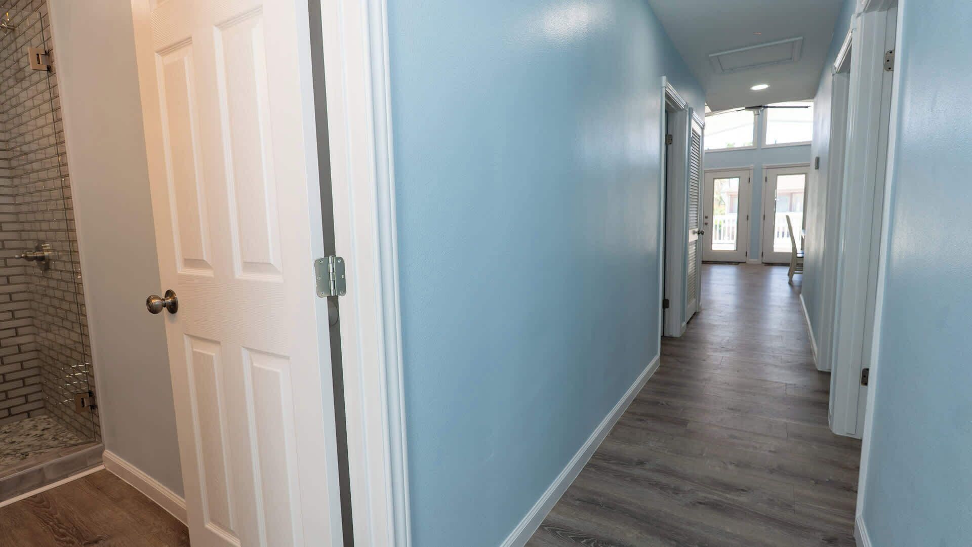 A hallway with a door on the left, a brick wall, and a light blue wall.