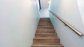 Un escalier en bois avec une rampe métallique, menant à un palier doté d’un mur bleu et d’un plafond blanc.