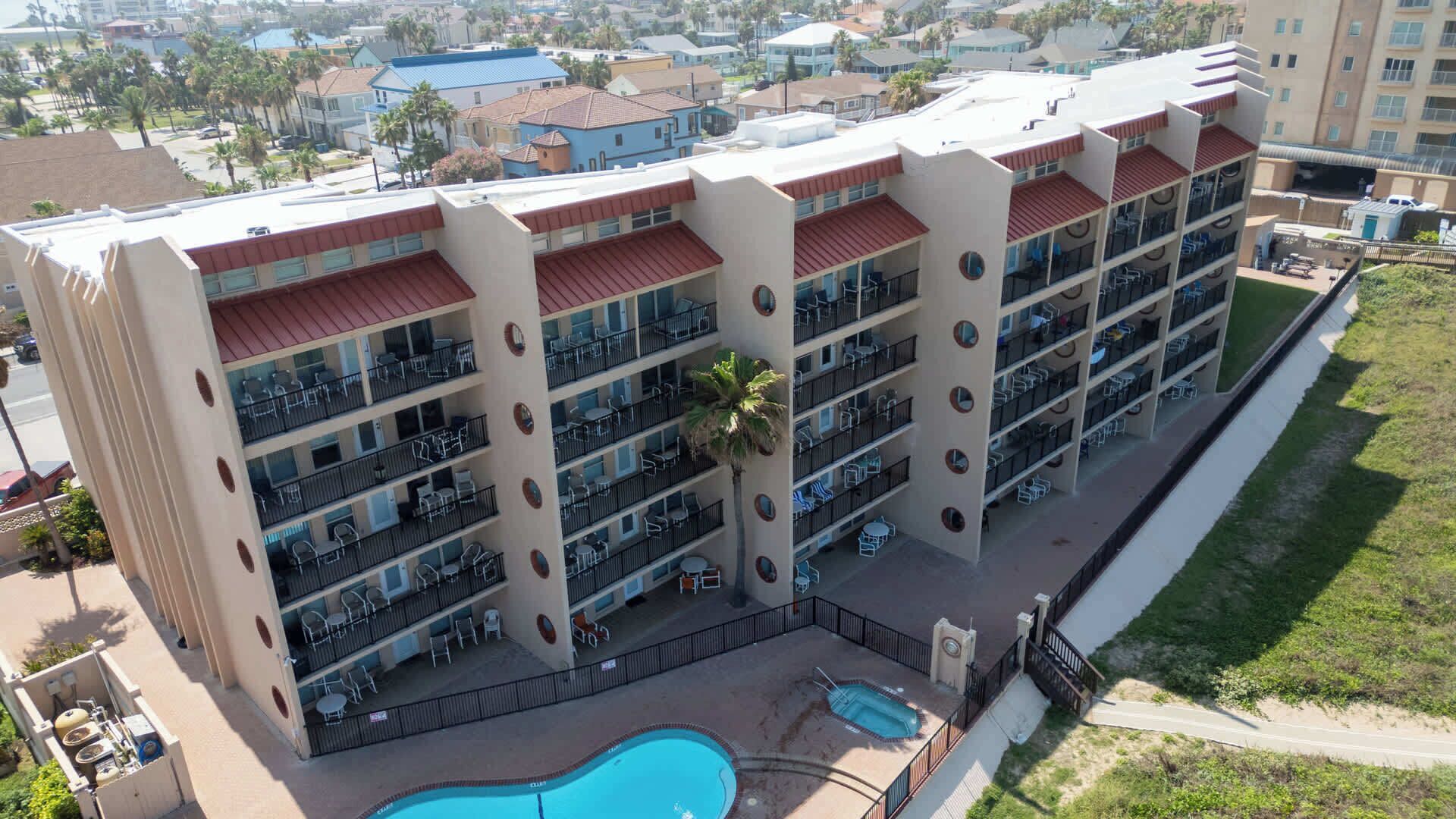 Um hotel com vários andares, varandas, piscina e vista do bairro ao redor.