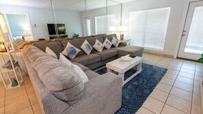 Ein Wohnzimmer mit einem Ecksofa, einem Couchtisch und einem Fernseher.