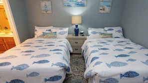 Quarto com duas camas, uma mesa de cabeceira, abajur e quadros nas paredes.