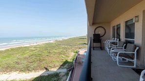 Uma varanda com vista para a praia, uma piscina e um espaço de estar com cadeiras.