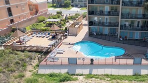 Una piscina en la azotea con sillones de descanso y sombrillas, rodeada por una cerca y edificios.