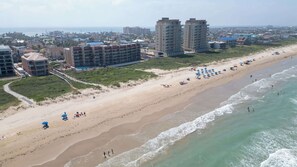 Ein Strand mit einer Reihe von Strandsonnenschirmen, einem Sandstrand und Gebäuden im Hintergrund.