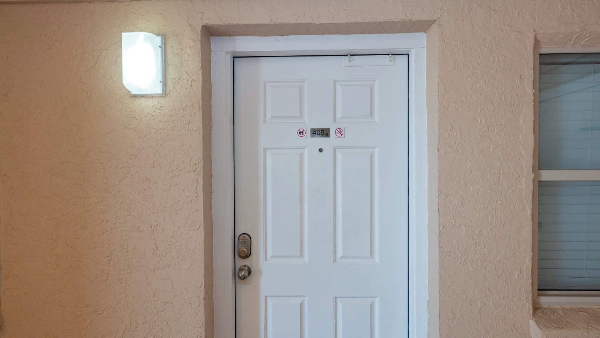 A white door with a number plate, a peephole, and a small light above it.