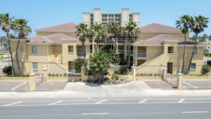 A multi-story hotel with a central courtyard, palm trees, and a tiled roof. - New 2BR - Pool Patio - Bunk Beds - 1st Floor (South Padre Island)