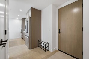 A hallway with a wooden door, a metal rack, and a kitchen area with cabinets and appliances.