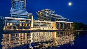 A waterfront hotel with modern architecture, a reflection in the water, and a night sky. - Luxury Beachfront | 2 Bed | Pool & Hot Tub | Gym (Kelowna)