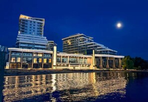 A waterfront hotel with modern architecture, a reflection in the water, and a night sky. - Luxury Beachfront | 2 Bed | Pool & Hot Tub | Gym (Kelowna)