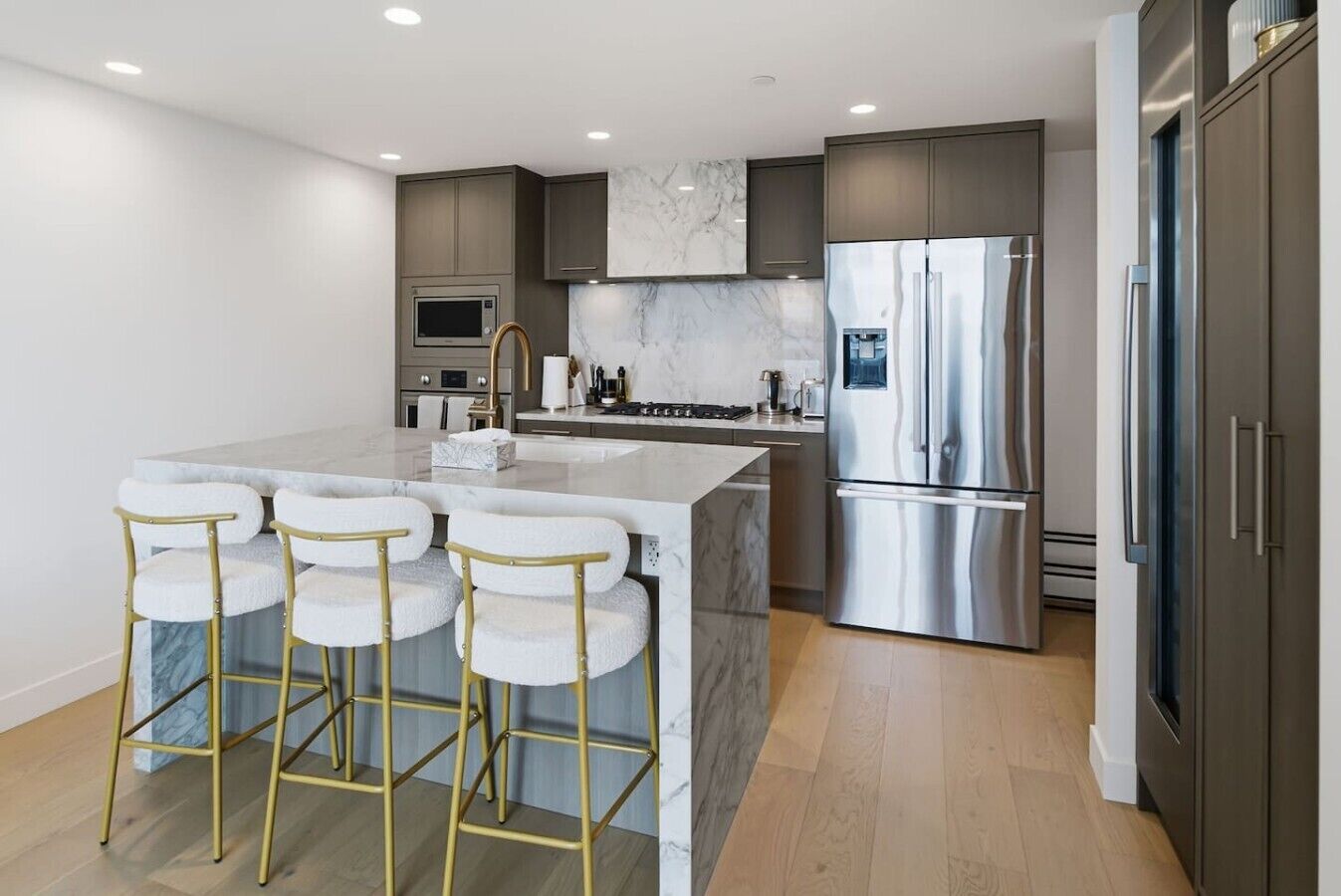 A modern kitchen with a marble island, stainless steel appliances, and bar stools.