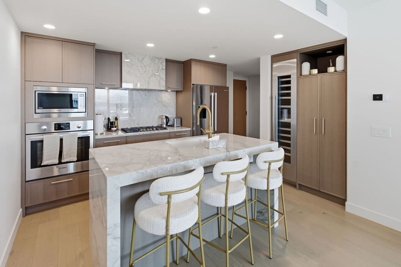A modern kitchen with a central island, stainless steel appliances, and a bar stool seating arrangement.