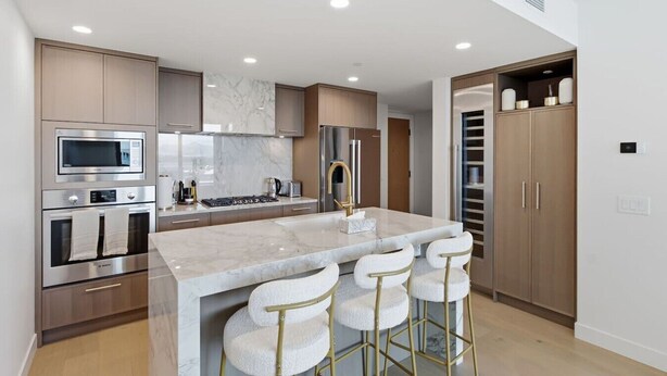 A modern kitchen with a central island, stainless steel appliances, and a bar stool seating arrangement. - Luxury Beachfront | 2 Bed | Pool & Hot Tub | Gym (Kelowna)