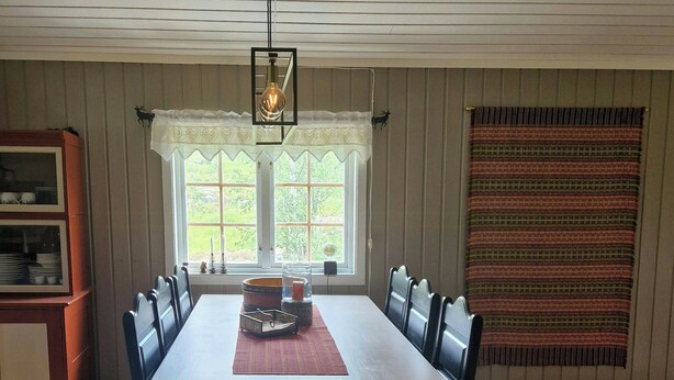 Ein Esszimmer mit einem langen Tisch, Stühlen, einem Teppich und einem Fenster mit Vorhängen.