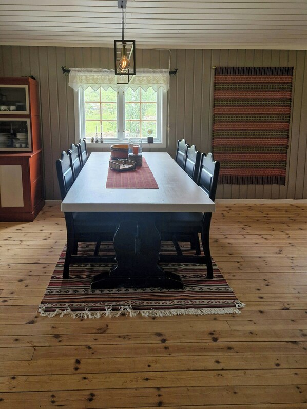 A dining room with a long table, chairs, a rug, and a window with curtains.