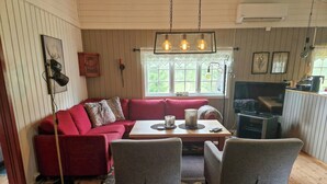 Ein gemütliches Wohnzimmer mit einem roten Sofa, grauen Sesseln, einem Holztisch und einem Fernseher.