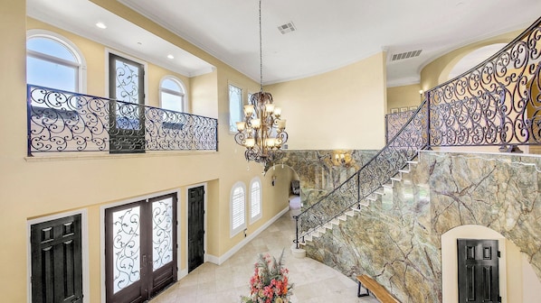 A spacious interior with a grand staircase, ornate railings, and a chandelier.