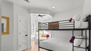 A bunk bed with white bedding, a ceiling fan, and a door with a yellow frame. - Luxury 7BR - Heated Pool, Hot Tub, Pet Friendly (Austin)