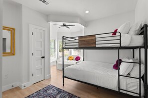 A bunk bed with white bedding, a ceiling fan, and a door with a yellow frame.