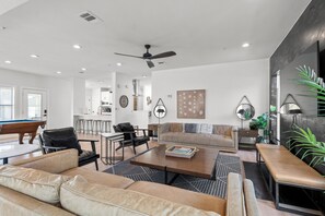 A modern living room with a pool table, leather sofas, a coffee table, and a dining area with bar stools.