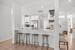 Una cocina moderna con armarios blancos, electrodomésticos de acero inoxidable y una isla central con taburetes.
