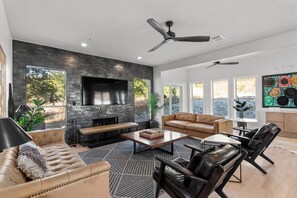 Una sala de estar moderna con chimenea, muebles de cuero y ventanas amplias que ofrecen vistas al exterior.