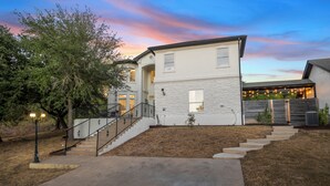 A two-story house with a stone facade, a front porch with a staircase, and a backyard with a wooden fence. - Luxury 7BR - Heated Pool, Hot Tub, Pet Friendly (Austin)