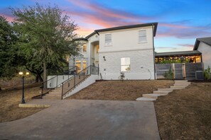 A two-story house with a stone facade, a front porch with a staircase, and a backyard with a wooden fence.