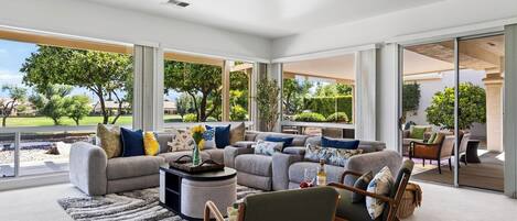 A spacious living room with a large sectional sofa, a coffee table, and a dining area visible through glass doors.