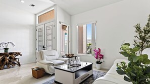 Un salon moderne avec un canapé blanc, une table basse en verre et une grande fenêtre.