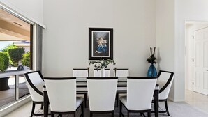A dining area with a white table and chairs, a framed artwork above the table, and a vase with a plant on the side. - Palm & Par by Avantstay Golf Views + Patio BBQ Mins to Indian Wells (Palm Desert)