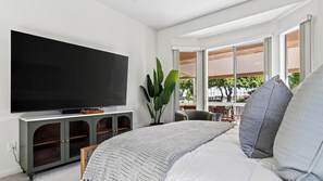 Un dormitorio con una cama grande, un televisor instalado en un mueble, una ventana con vistas al exterior y una planta.