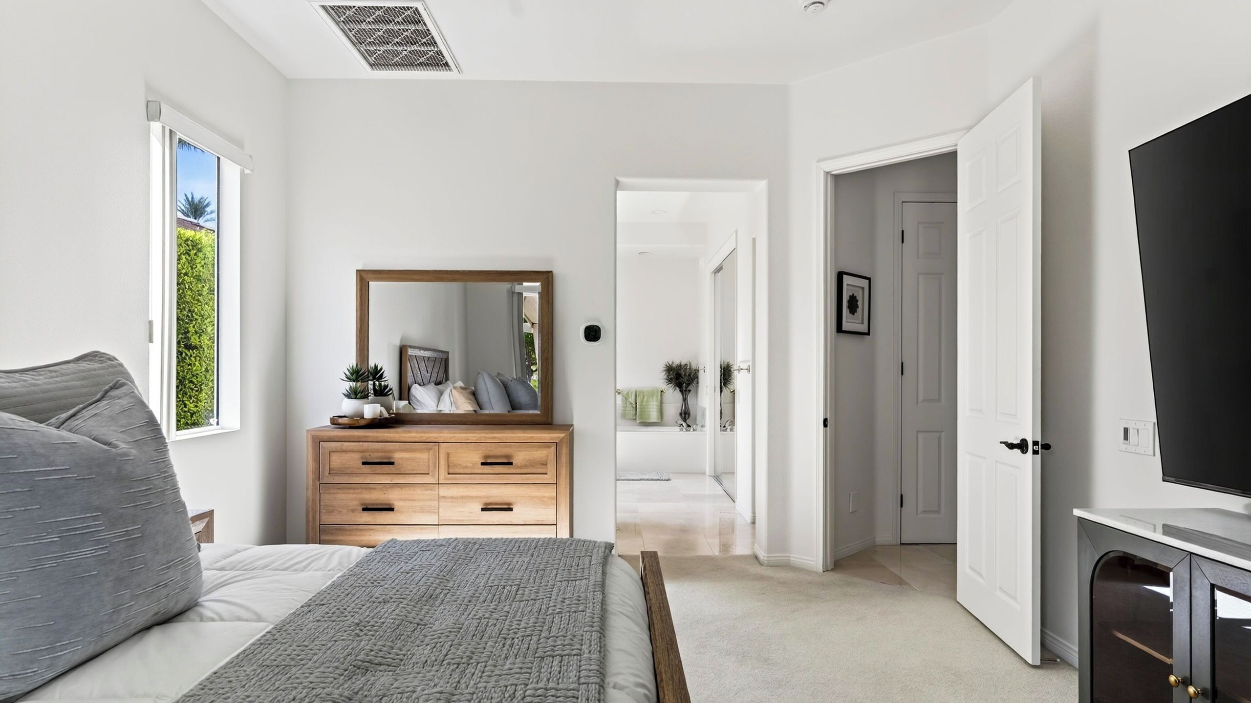 A bedroom with a bed, a dresser, a mirror, and a TV.