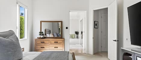 A bedroom with a bed, a dresser, a mirror, and a TV.