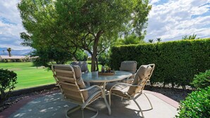 An outdoor patio with a round table and four chairs, surrounded by a well-maintained hedge and a tree. - Palm & Par by Avantstay Golf Views + Patio BBQ Mins to Indian Wells (Palm Desert)
