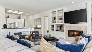 Una sala de estar moderna con chimenea, televisor de pantalla plana y zona de cocina con armarios blancos.